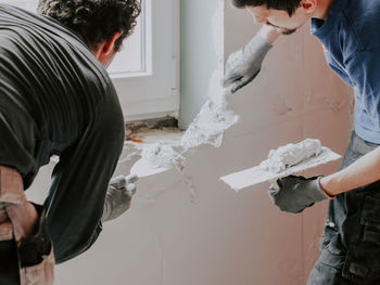 Young caucasian guys plasterers apply putty with spatulas on the wall