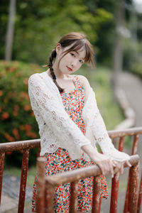 Portrait of young woman standing by railing