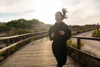 Active young female in black sportswear jogging on wooden pathway during outdoor fitness training in nature