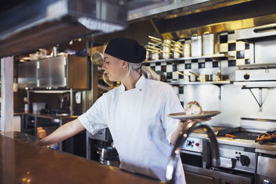 Female chef holding plate in kitchen at restaurant