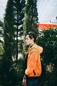 Young woman looking away while standing by trees against plants