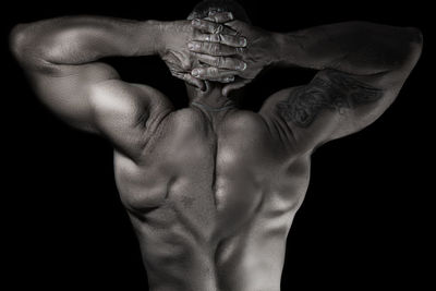 Close-up of shirtless man flexing muscles against black background