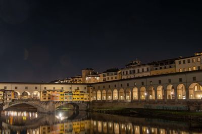 Illuminated bridge over river by buildings against sky at night