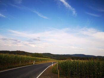 Empty road amidst field against sky