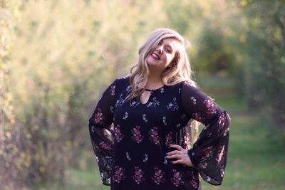 Portrait of smiling woman with hands on hip standing against trees