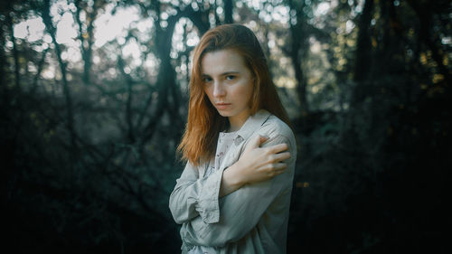 Portrait of young woman standing against trees