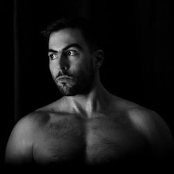 Shirtless young man looking away against black background