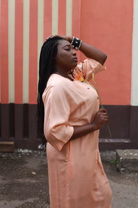 Side view of young woman standing on road against wall