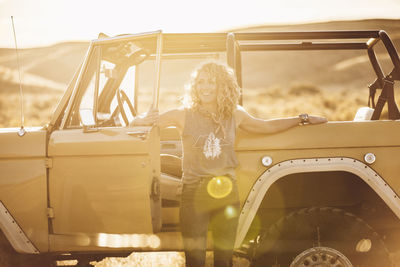 Cheerful woman looking away while standing against off-road vehicle during sunny day