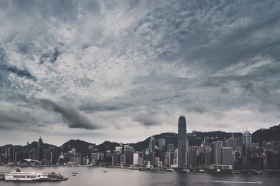 View of cityscape by river against cloudy sky