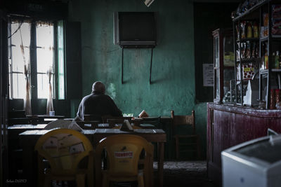 Rear view of man sitting on chair in abandoned building