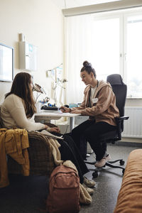 Full length of non-binary school nurse discussing with female student in office