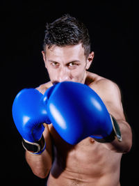 Portrait of shirtless male boxer standing against black background
