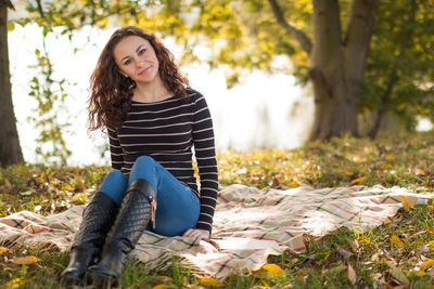 Full length portrait of woman smiling while sitting on picnic blanket at park