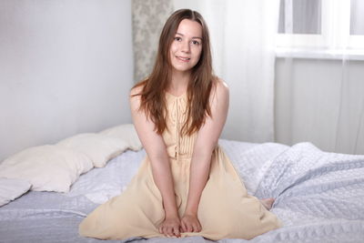 Portrait of smiling young woman sitting on bed at home