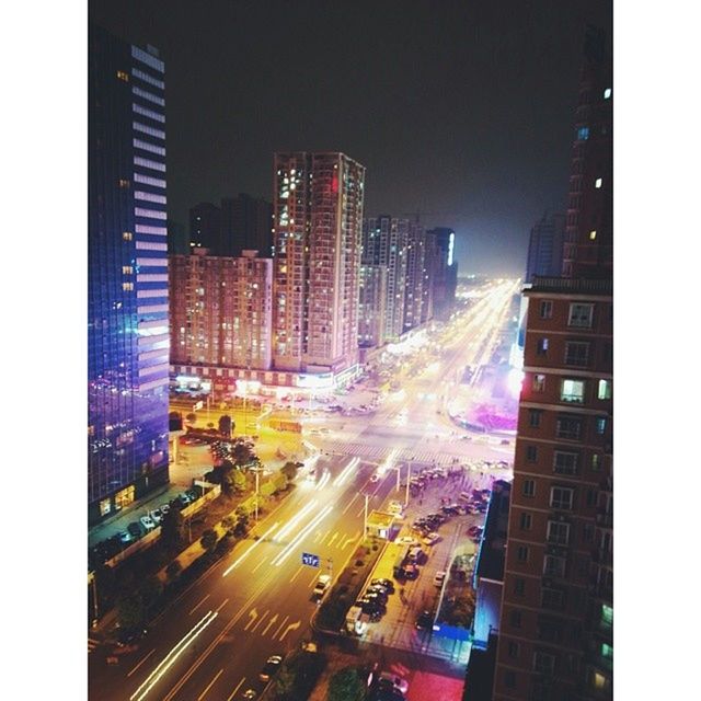 city, illuminated, building exterior, architecture, night, built structure, skyscraper, cityscape, long exposure, light trail, transportation, traffic, city life, road, motion, street, modern, office building, tall - high, car