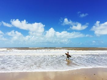 Man with surfboard walking on shore at beach against sky