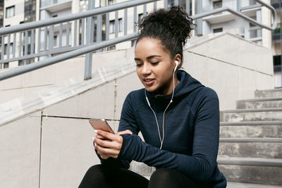 Young woman listening music through mobile phone while sitting on steps