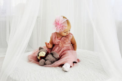 Cute girl with stuffed toy sitting on bed