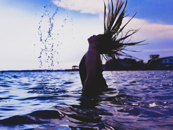 Woman splashing water in sea against sky