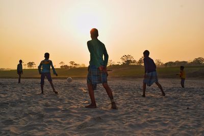 People playing on beach against sky during sunset