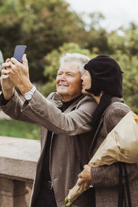 Woman kissing senior man taking selfie through smart phone during weekend