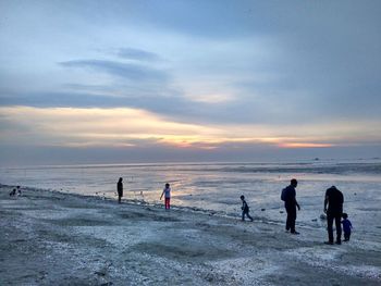 Silhouette people standing on beach against sky during sunset