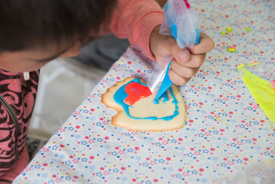 High angle shot boy decorating homemade colorful cookie