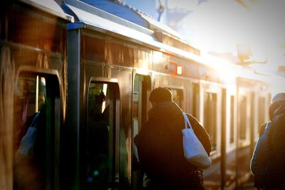 Rear view of man standing by train at platform during sunny day