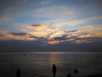 Silhouette people on beach against sky during sunset