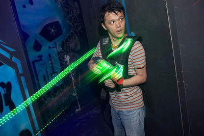 Full length of young man standing against illuminated wall at night