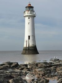 Lighthouse on rock by sea against sky