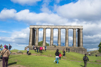 Group of people in front of historical building against cloudy sky