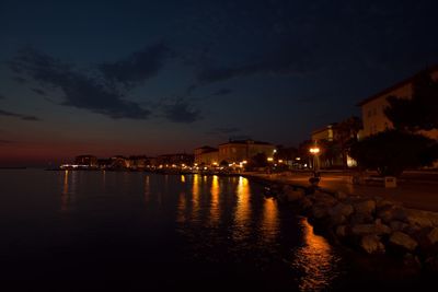 Illuminated buildings by river against sky at night