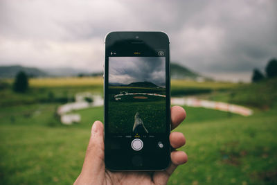 Close-up of hand holding smart phone against sky