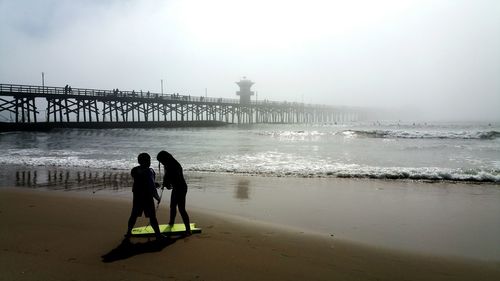 People with paddleboard on beach against ocean and foggy sky