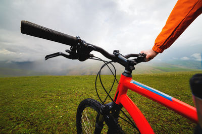 Low section of man riding bicycle on field against sky