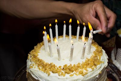 Cropped image of hand lighting birthday candles on cake