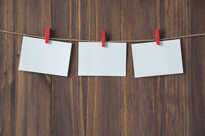 Close-up of blank papers hanging with clothespins on string against wooden wall