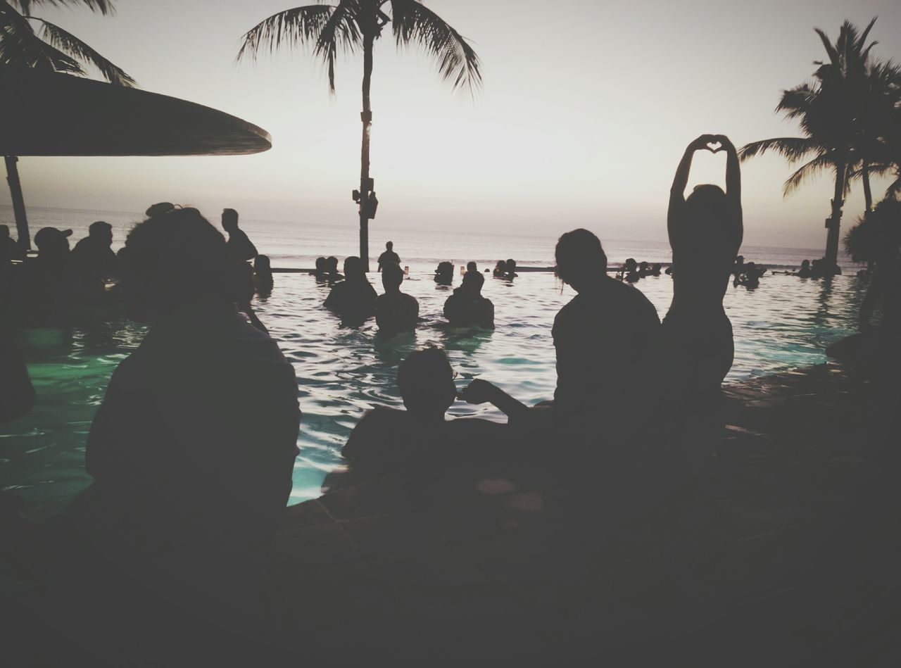 water, sea, sky, silhouette, group of people, tropical climate, real people, nature, beach, leisure activity, palm tree, lifestyles, land, tree, sitting, beauty in nature, relaxation, men, women, horizon over water, outdoors