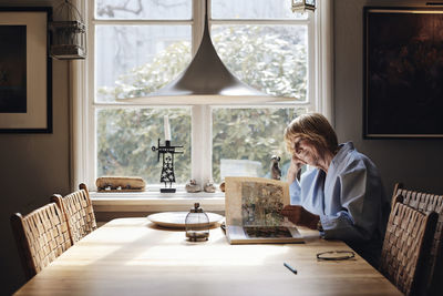 Smiling senior woman looking at picture book on dining table at home