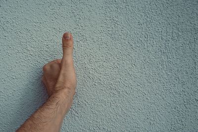 Close-up of hand gesturing thumbs up against wall outdoors