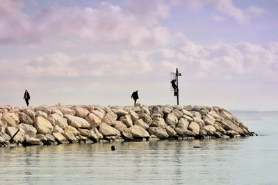 People standing on rock by sea against sky