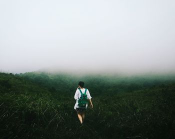 Rear view of man walking on field in foggy weather