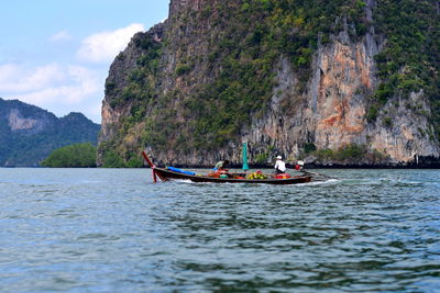 People with vegetables sitting on boat in sea against mountains
