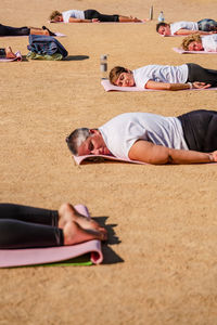 Side view of calm women in activewear lying on mats on ground after yoga session in park in sunlight