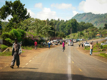 People on road by trees against sky