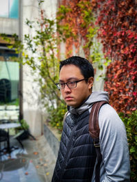 Portrait of young man looking away against red ivy covered wall.