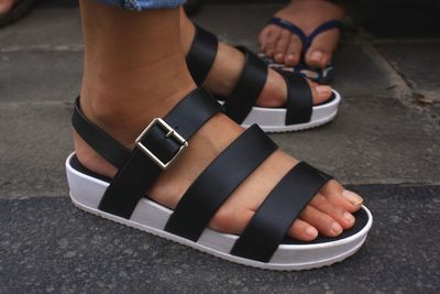 Low section of woman wearing sandals standing on footpath