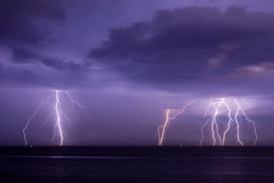 Firework display over sea against dramatic sky